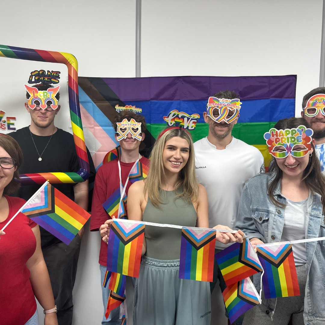 A group of people celebrating pride, holding LGBTQ+ rainbow flags.