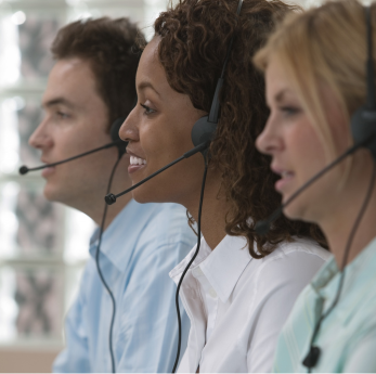 Three call centre workers wearing telephone headsets sit in a row, smiling and speaking with custome
